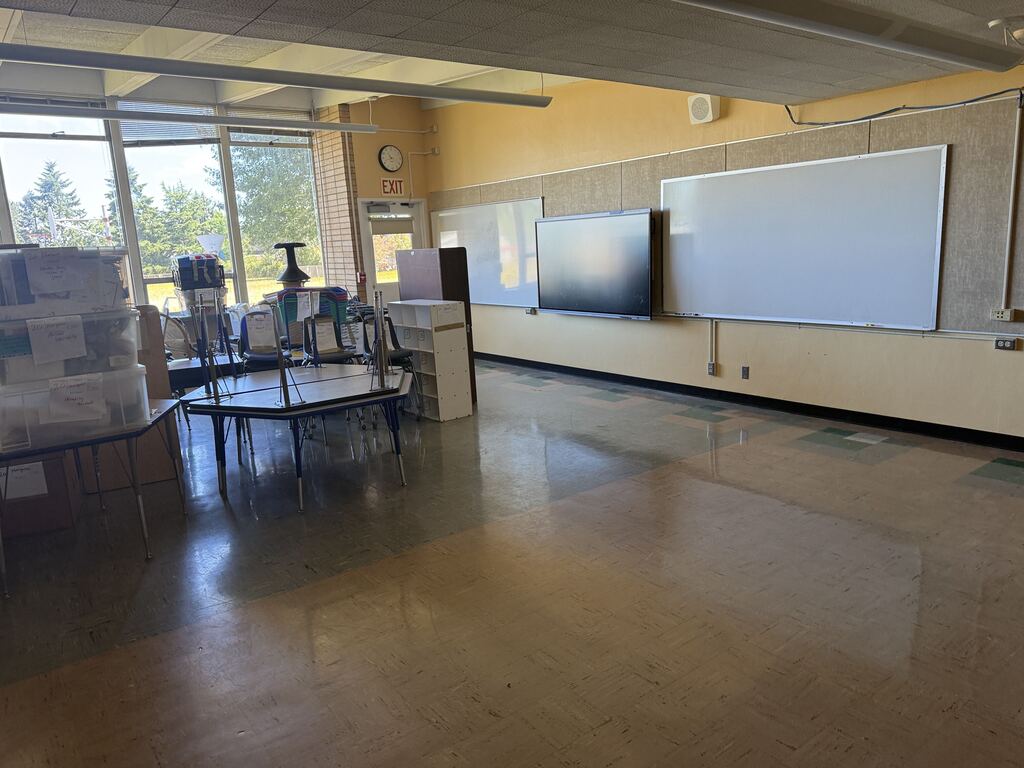 A classroom with furniture being stored and a white board and monitor hanging on the wall.