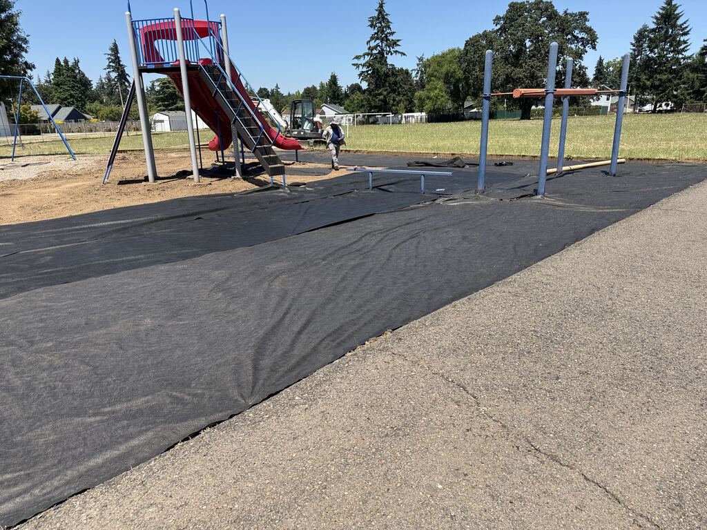 A playground with black plastic laid down getting ready for bark chips to be delivered.