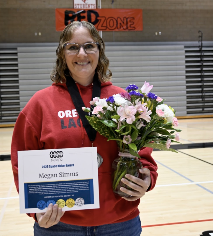 Megan Simms standing with flowers and award certificate with glasses and mid length blonde hair