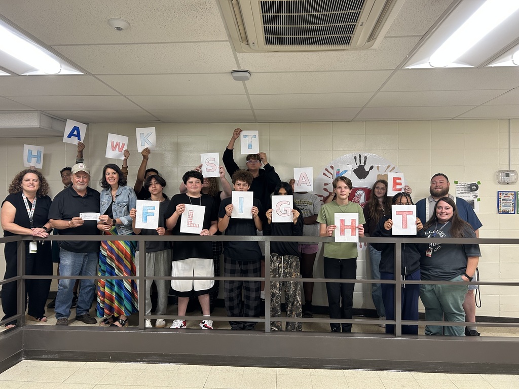 A group of students holding "Hawks Take Flight" Signs receiving a donation check