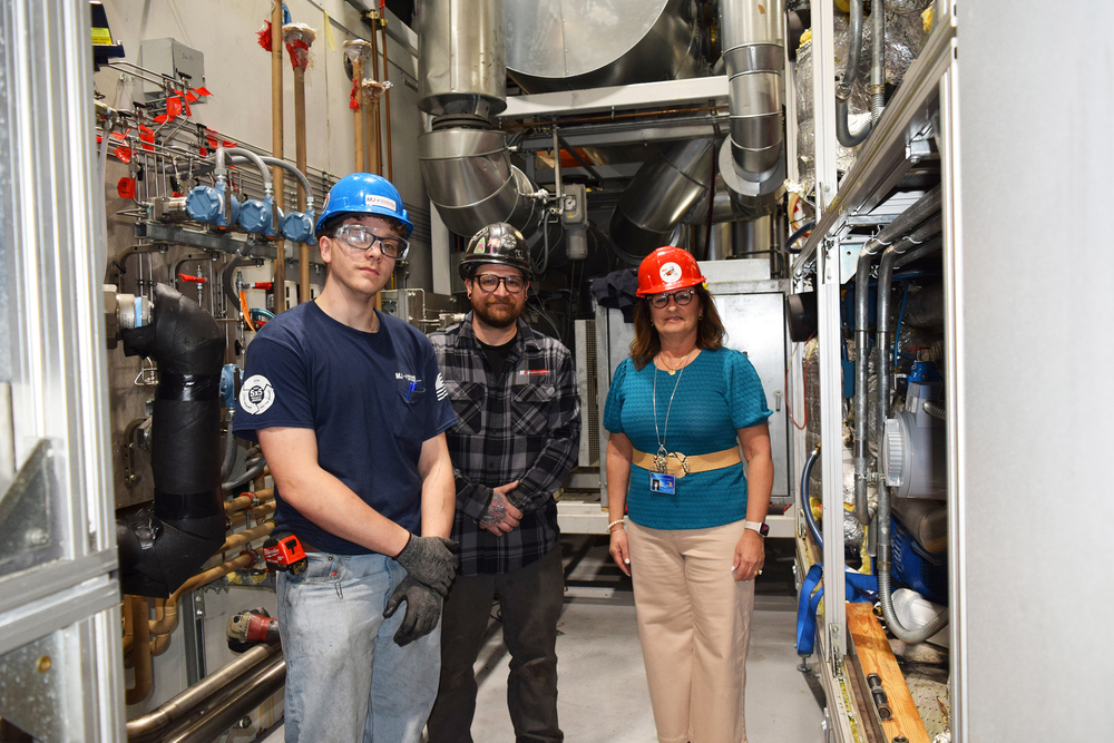 Three people stand in front of an HVAC system