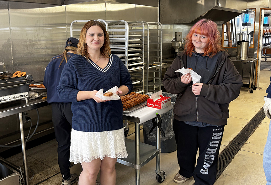 Two students holding doughnuts in a kitchen