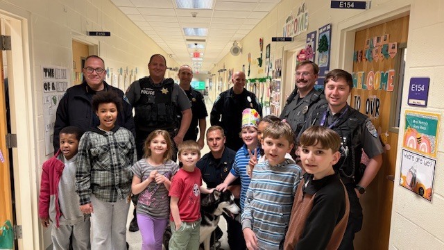 Police officers and dog posing with students in hallway
