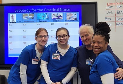 Three Practical Nursing students and their teacher pose in front of board with questions