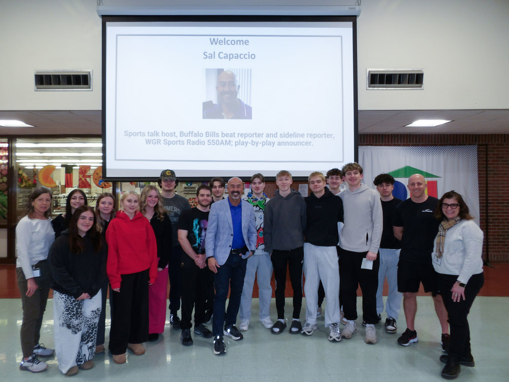 Students and staff pose with guest speaker Sal Capaccio in front of a presentation screen highlighting his role as a Buffalo Bills reporter and sports radio host.