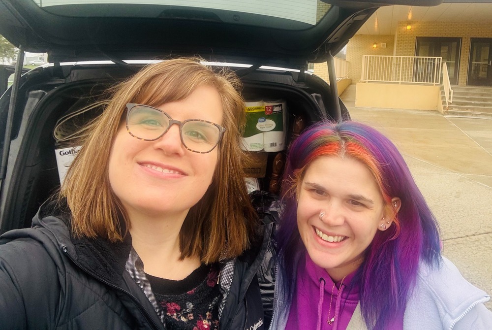 Two staff members posing in back of car