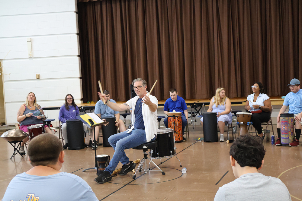 Man holding drum sticks talking to drum circle students