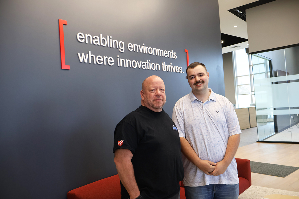 Two men standing front of sign in lobby of company