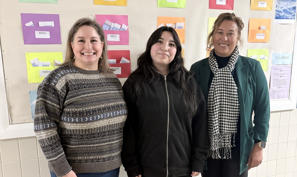 Two administrators standing with student in front of bulletin board