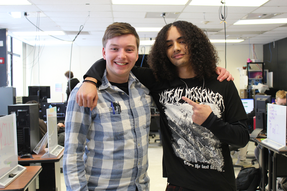 Two students one with his arm around the other and pointing at him