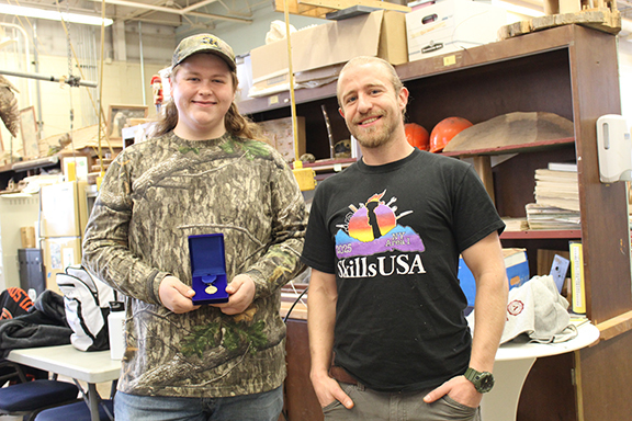 Student holding medal standing next to teacher