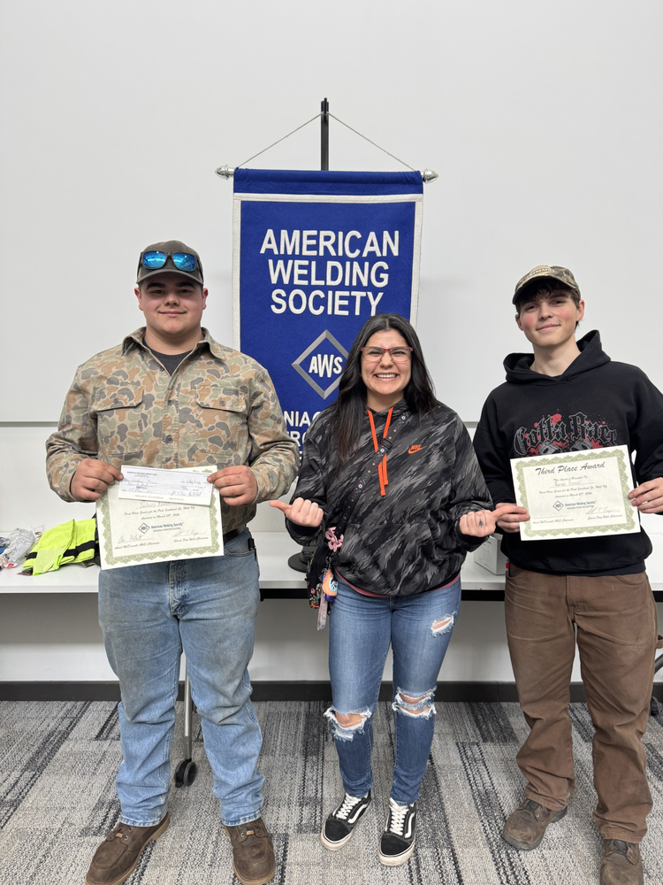 Two welding students with certificates posing with teacher