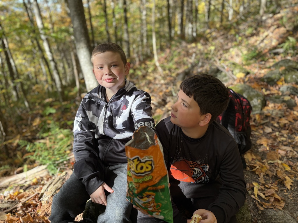 Two boys sittingon a rock and sharing a bag of Jalapeño cheetos