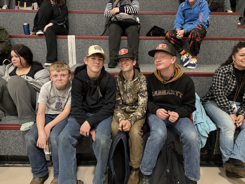 Three 8th graders and one 5th grader smiling at the camera on the bleachers