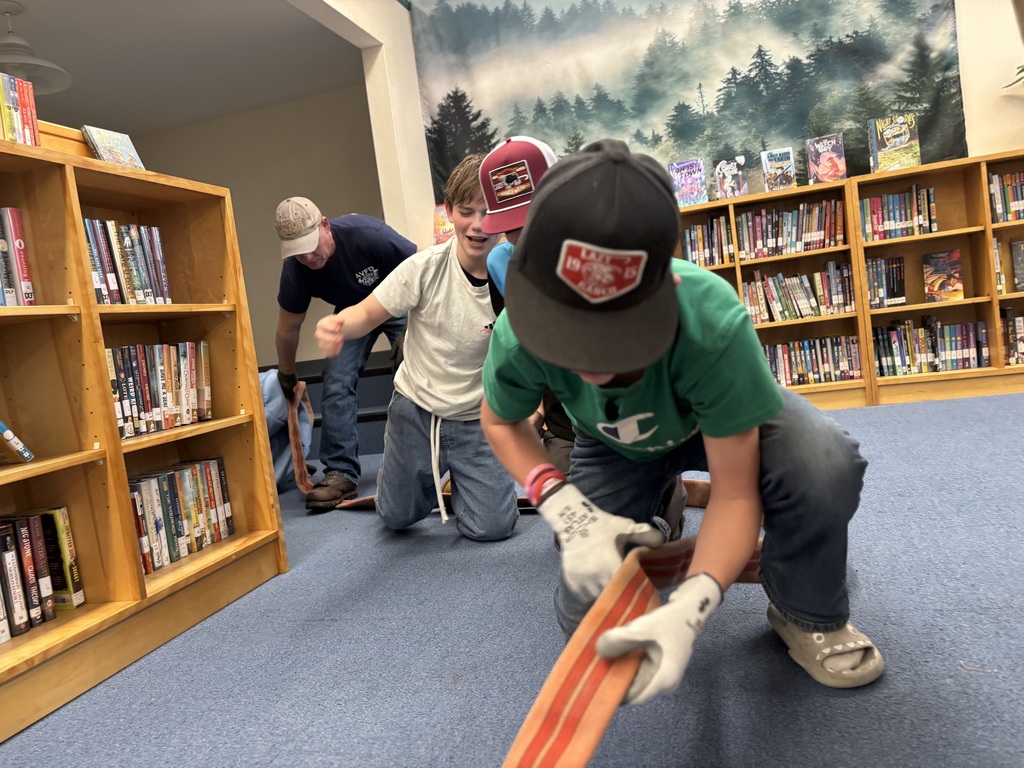 Two male students hold a fire house and have their blindfolds one while moving on one knee while they go to rescue a person in a "smoke-filled building"
