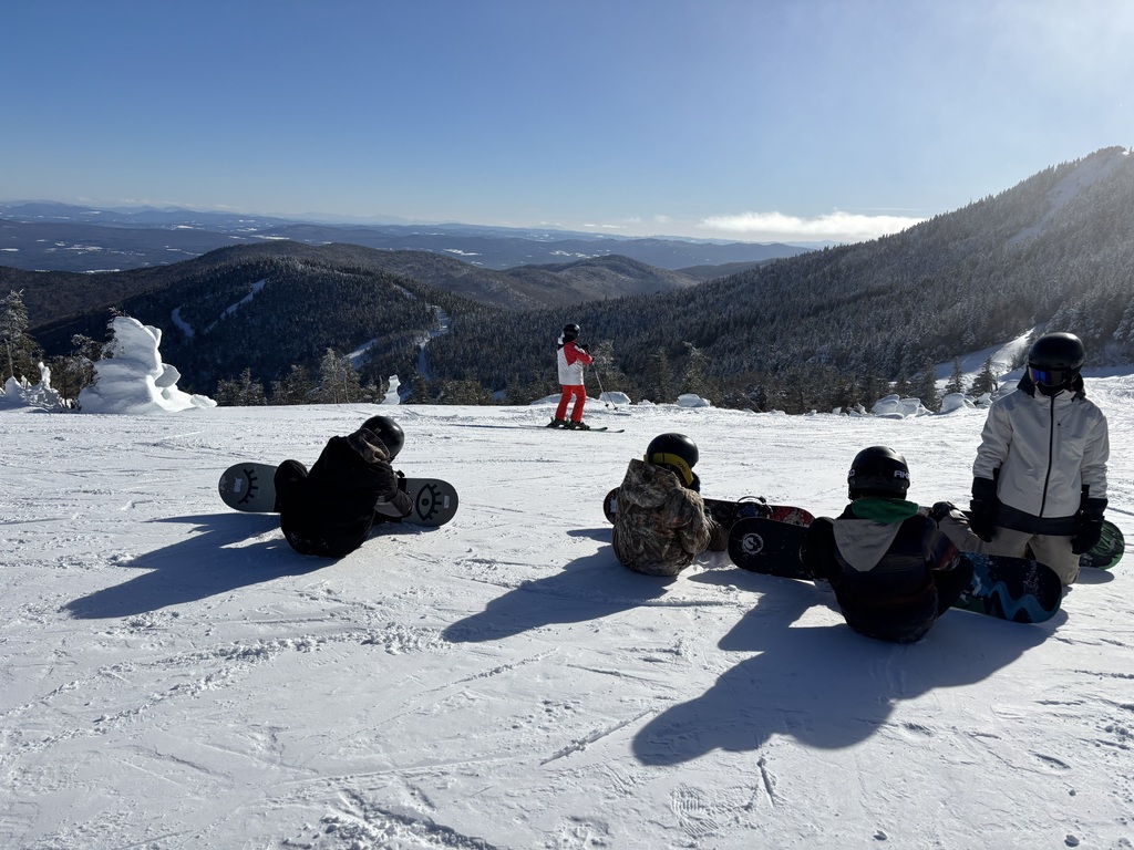 Four snowboarders are strapping in at the top of the Mountain at Jay Peak