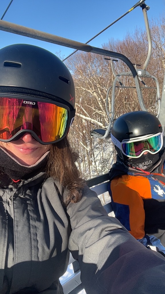 mother and son on the ski lift with their helmet and goggles on. 