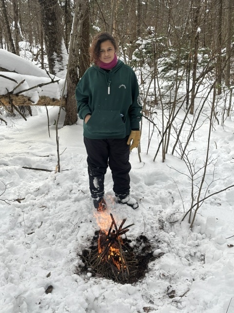 A student standing in front of an outdoor fire built in the snow