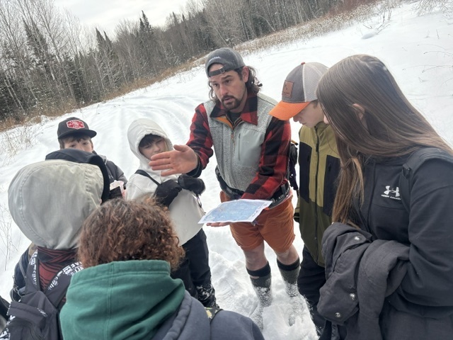 Devin looking at a map outside with a circle of  students