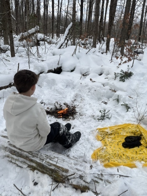A student sitting in front of an outdoor fire outside