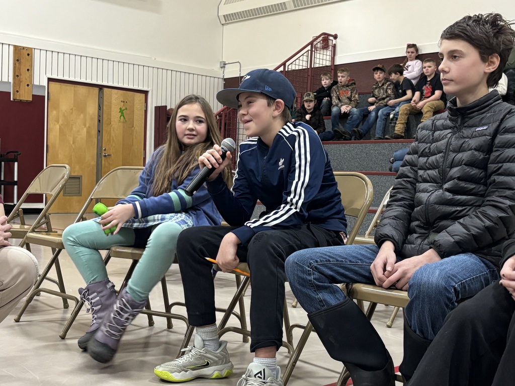 finalist spells a word into the mic while his two competitors watch