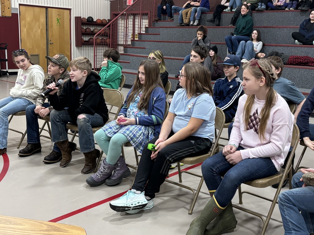 spelling bee competitors sitting in chairs, while one 5th grade correctly spells the given word. 