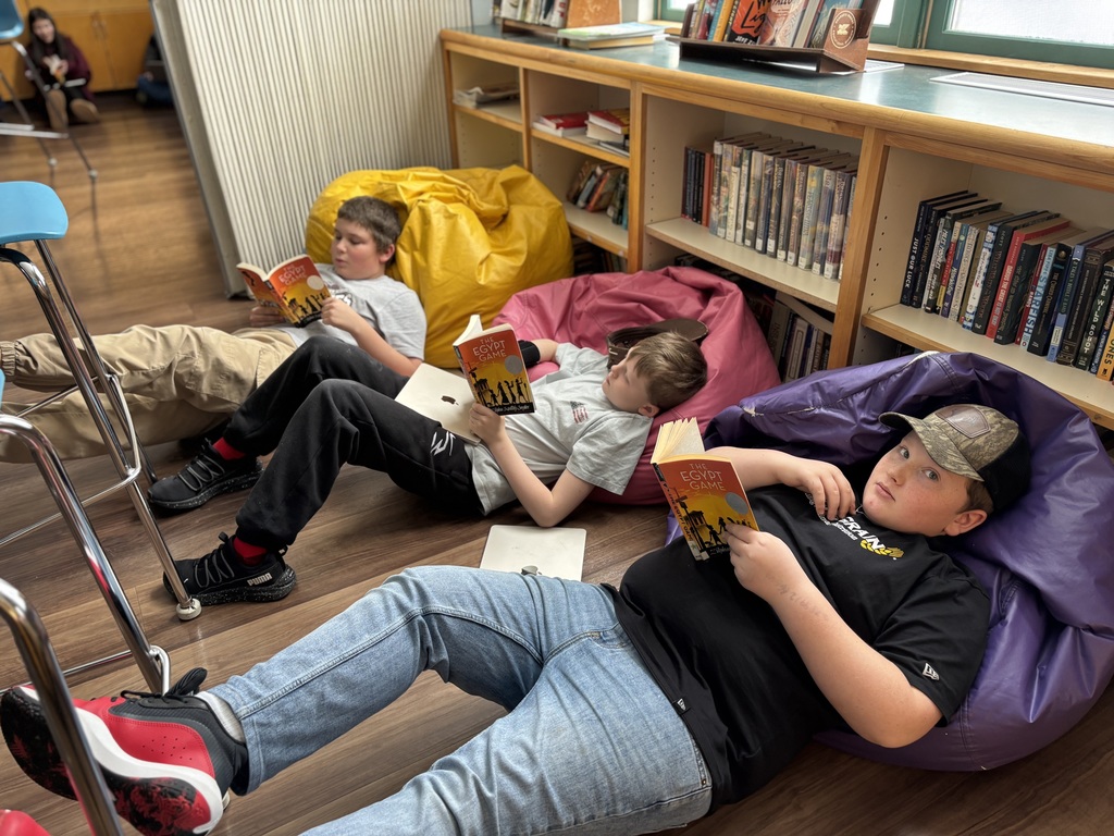 Three 6th grade boys lie in bean bags and read the Egypt Game 