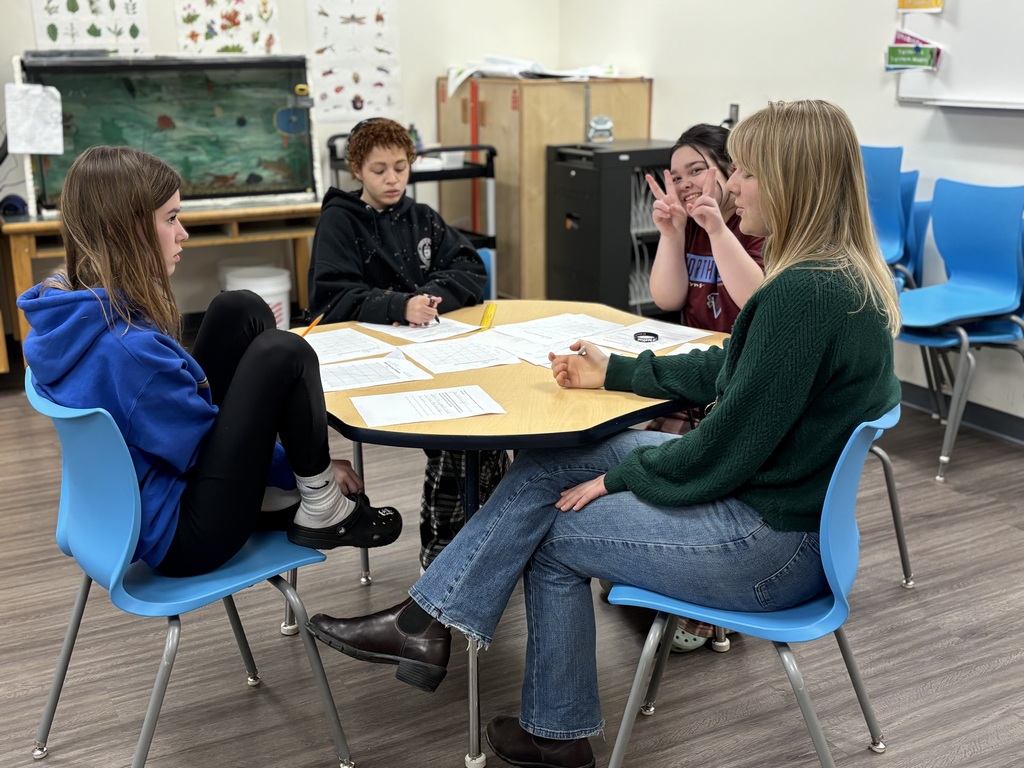Ms. Deonigi goes over some science work with three 8th grade girls at a small table. 