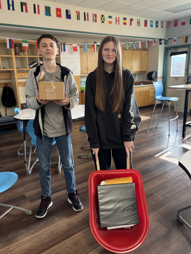 An 8th grade boy carries a box and an 8th grade girl carries her wheelbarrow