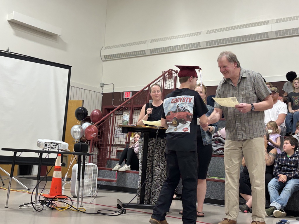 an 8th grade boy shakes with with board member Dan Rook as he hands him his graduation certificate