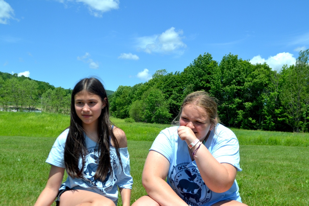 A 6th grade and a 7th grade girls sit in the field and chat 