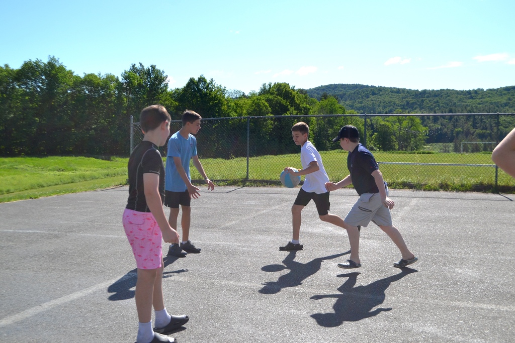 a group of 7th grade boys play basketball on the blacktop outside 