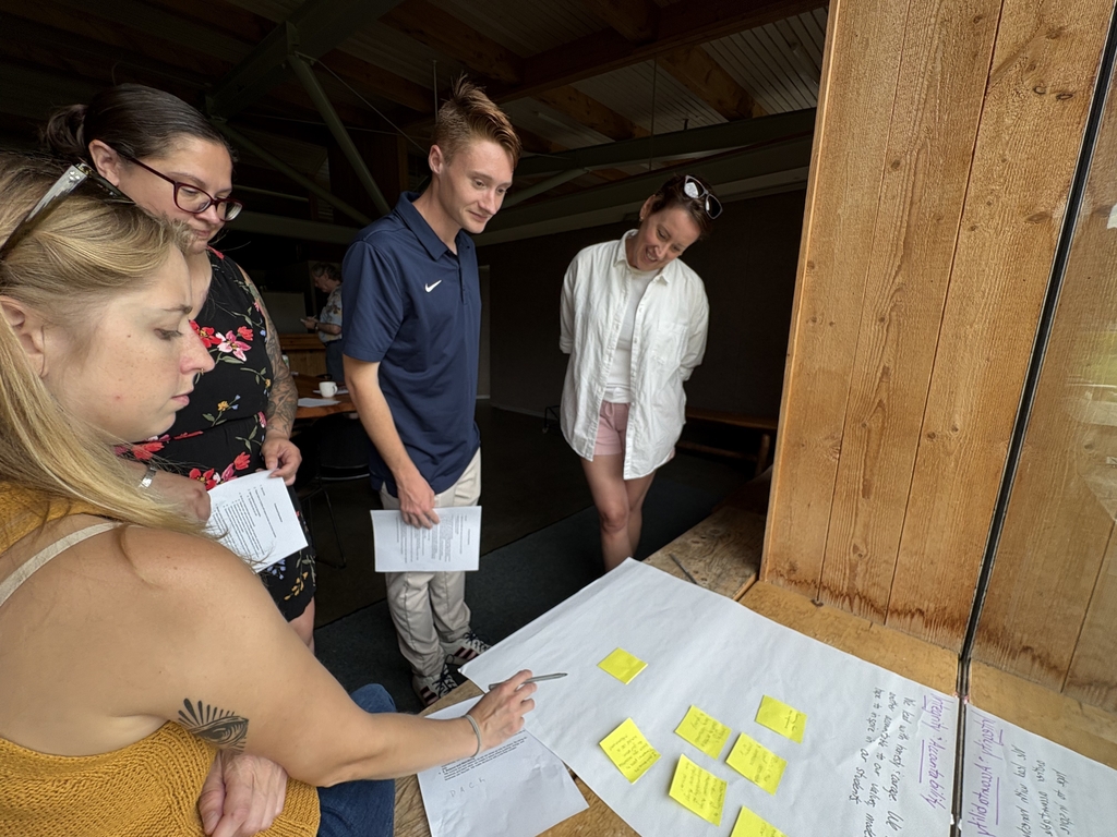 Teachers meet around a poster paper and sticky notes