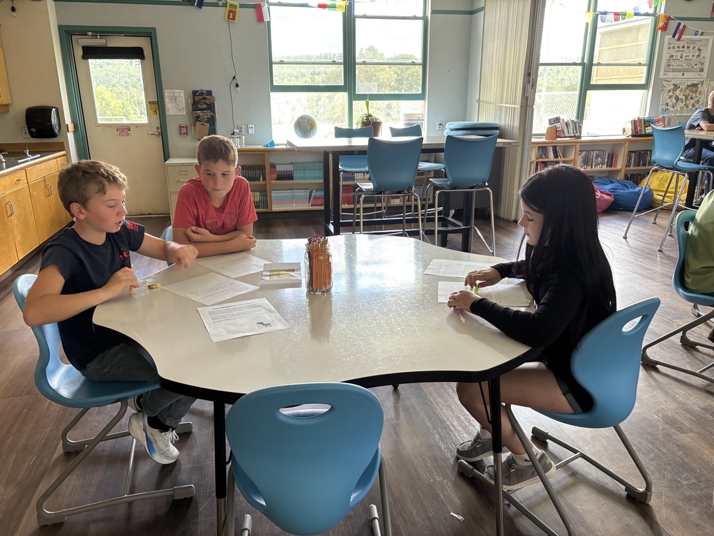 three 6th grades are gathered around the whiteboard table reading case files