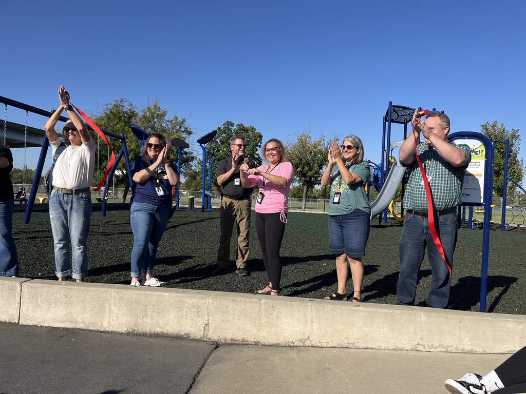 Photo of staff members holding  a red ribbon as they are cutting it for the grand opening of our playground equipment