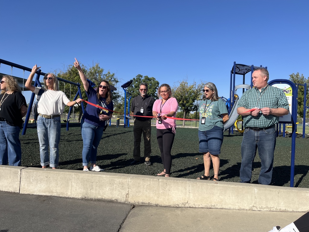 Photo of staff members holding  a red ribbon as they are cutting it for the grand opening of our playground equipment
