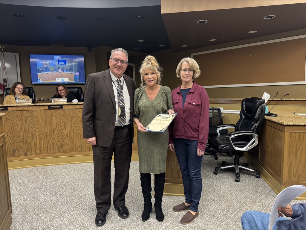 Woman in green dress being recognized for her jacket contributions with Dr Holtom on her right and another non profit member to her left in a burgundy jacket.