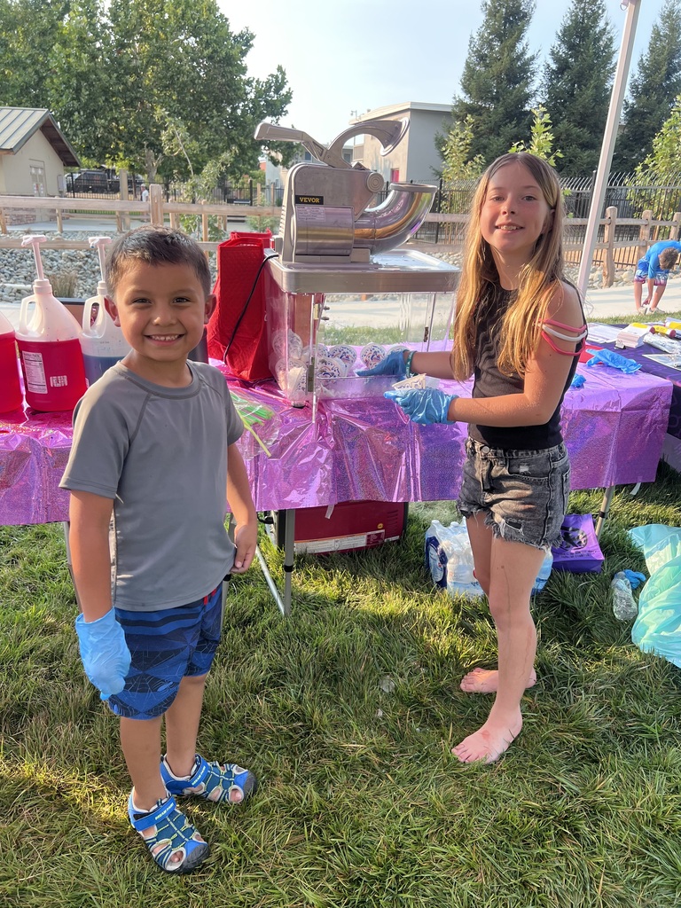 Two children in gloves, one in shorts and the other in a t-shirt, standing next to a table.
