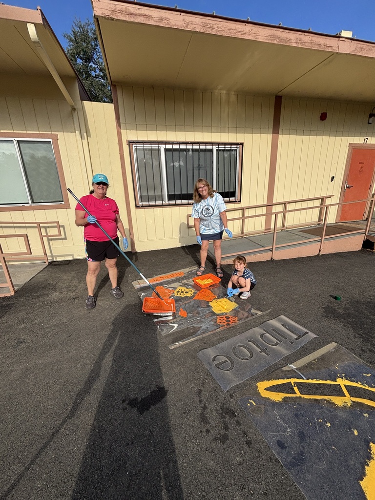 Three people stand in front of a building. One holds a cleaning tool, and the others are near a small child.