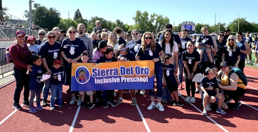 A group of people stands on a running track. Many wear blue shirts, and some hold a banner.