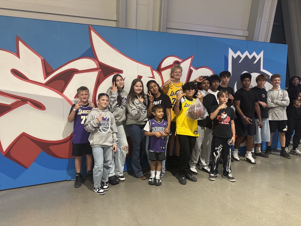 A group of people stand in front of a large, colorful graffiti-style wall, smiling and posing for a photo.