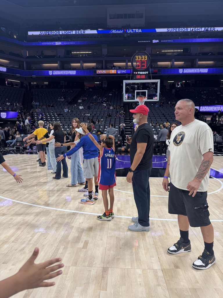 Basketball court with players and coaches. A player in a blue jersey holds hands with a child.
