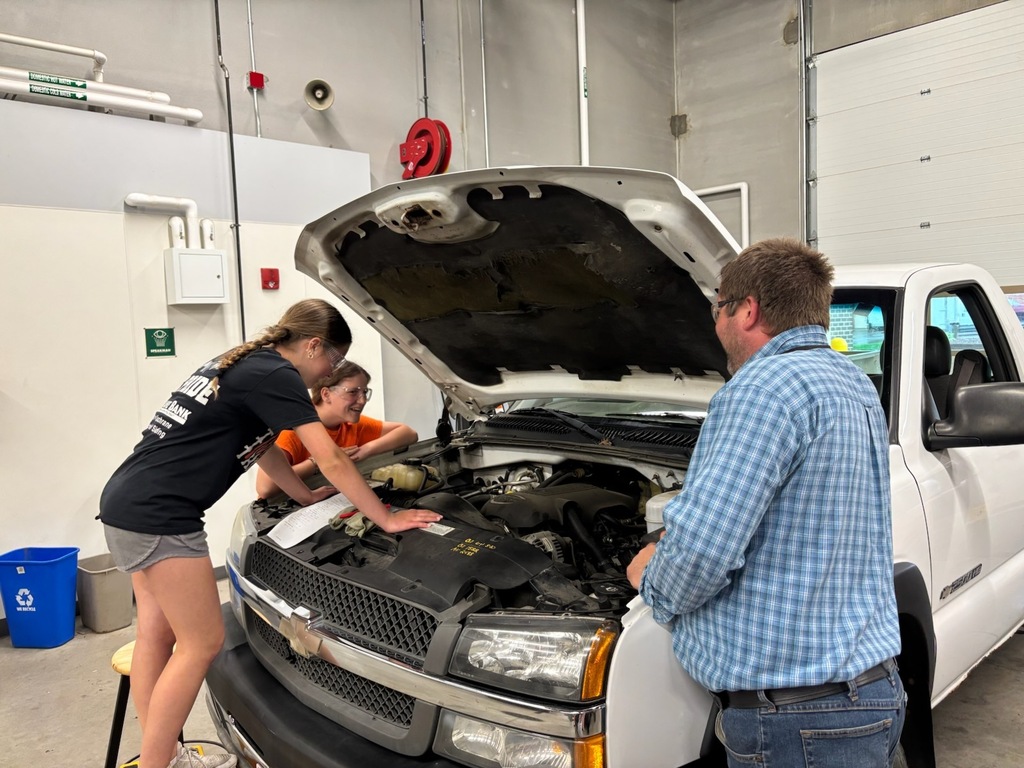 students and teacher looking under the hood of a truck