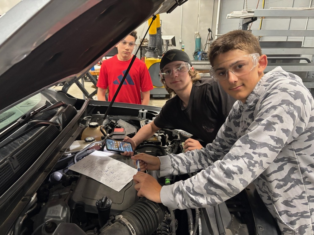 three students working on a car engine.