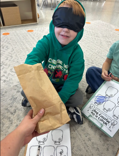 Blindfolded student reaching into a paperbag