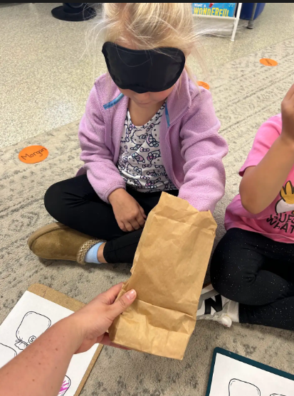 Blindfolded student reaching into a paperbag