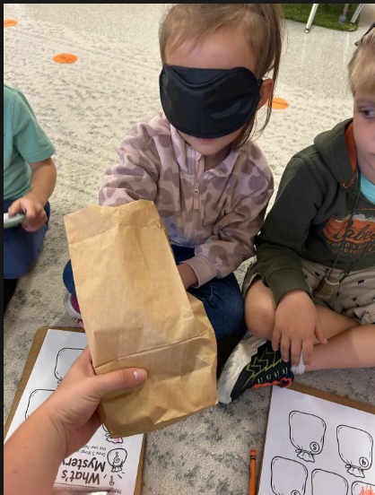 Blindfolded student reaching into a paperbag