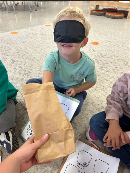 Blindfolded student reaching into a paperbag