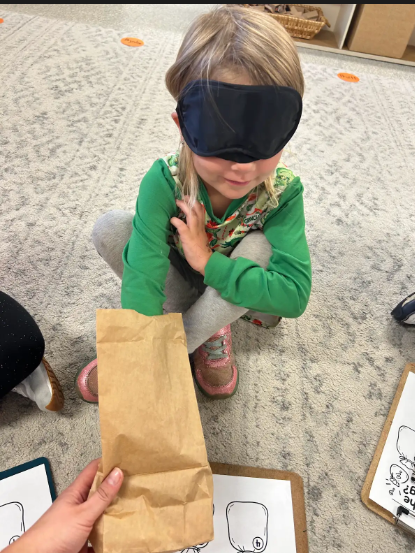 Blindfolded student reaching into a paperbag