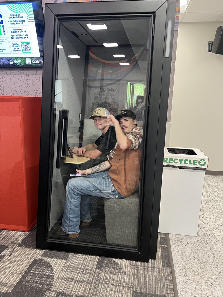 Two students sitting in a sound proof booth One giving a thumbs down